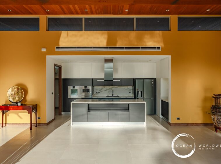 Modern kitchen with an orange accent wall, white and gray cabinets, stainless steel appliances, and a central island in an open-plan space.