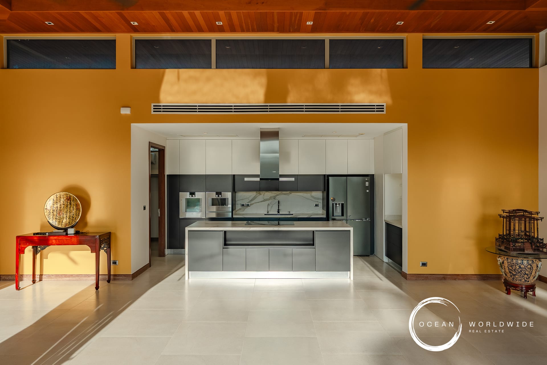 Modern kitchen with an orange accent wall, white and gray cabinets, stainless steel appliances, and a central island in an open-plan space.
