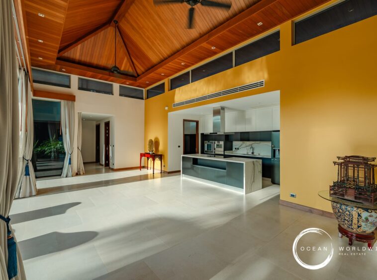 Open-plan living area with a yellow accent wall, white kitchen and a warm wood vaulted ceiling.