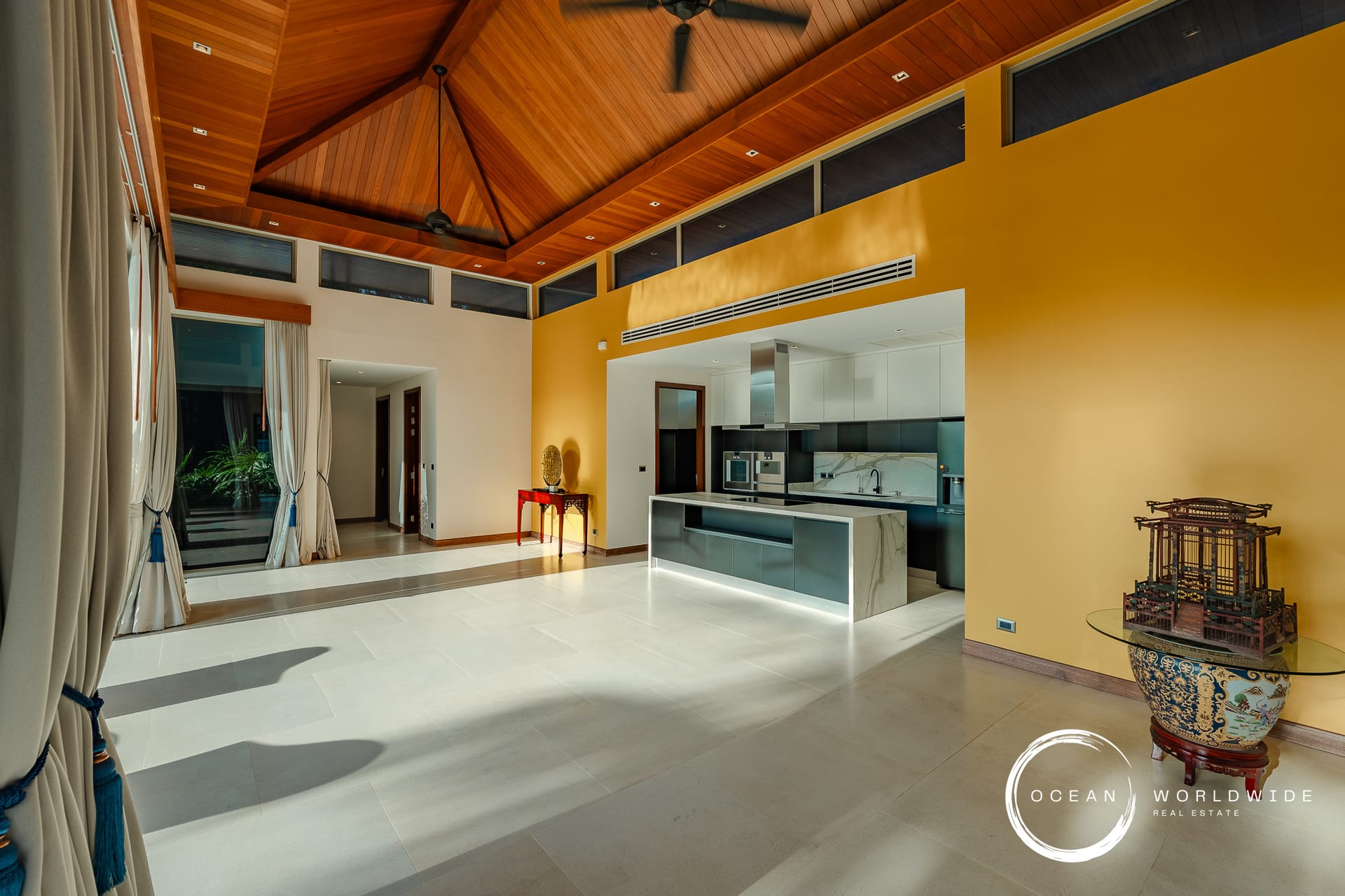 Open-plan living area with a yellow accent wall, white kitchen and a warm wood vaulted ceiling.
