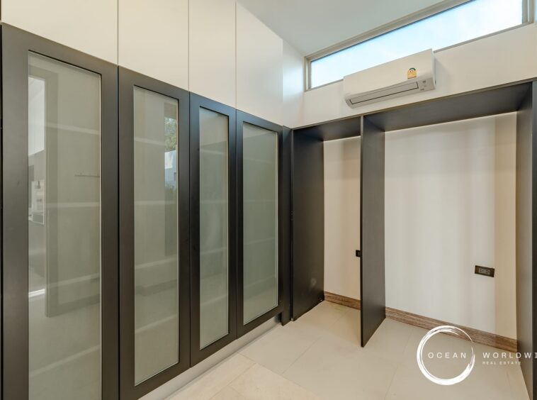 Modern elevator lobby with glass-fronted doors and dark frames, white walls, and a high window.