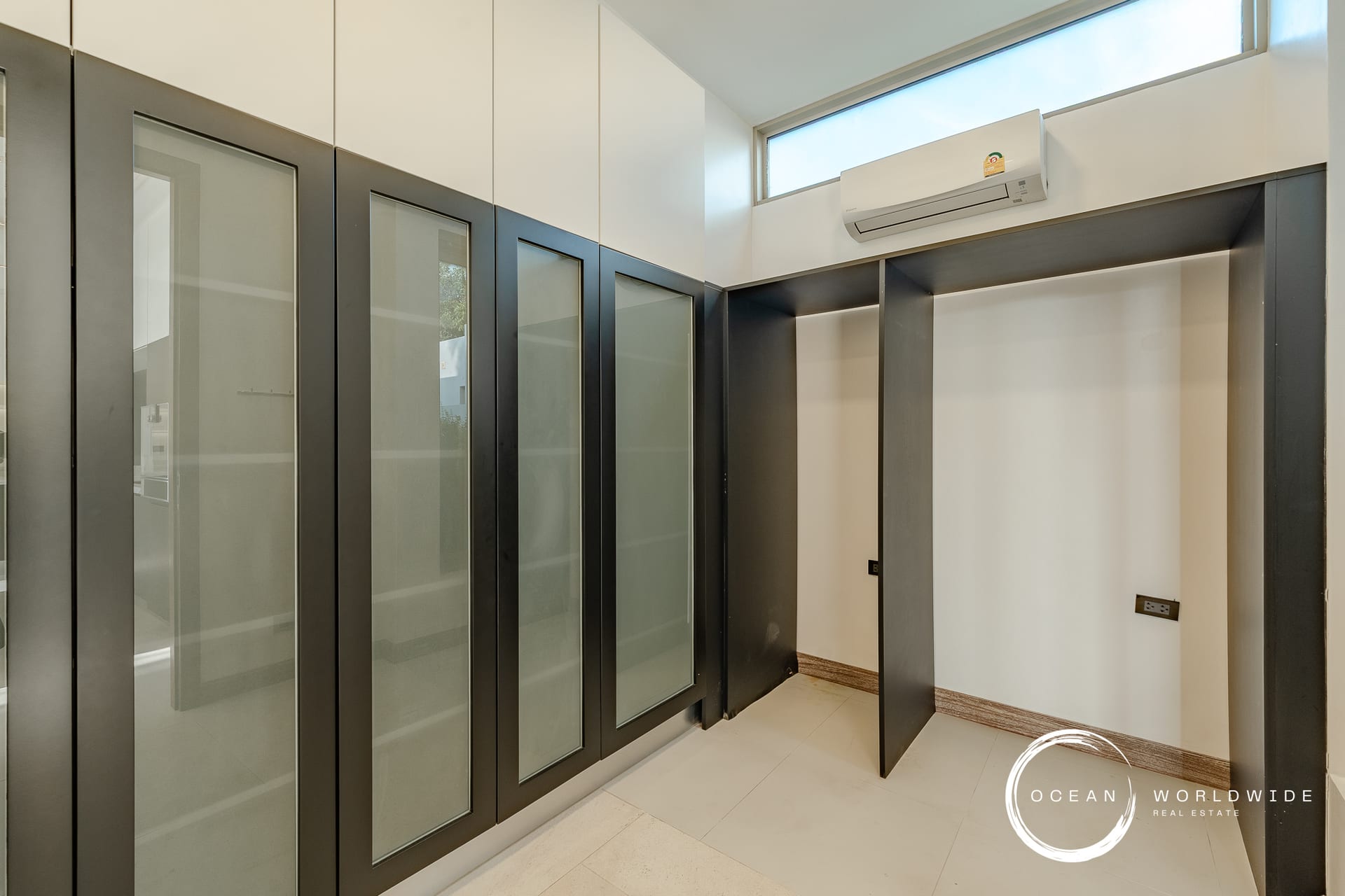Modern elevator lobby with glass-fronted doors and dark frames, white walls, and a high window.