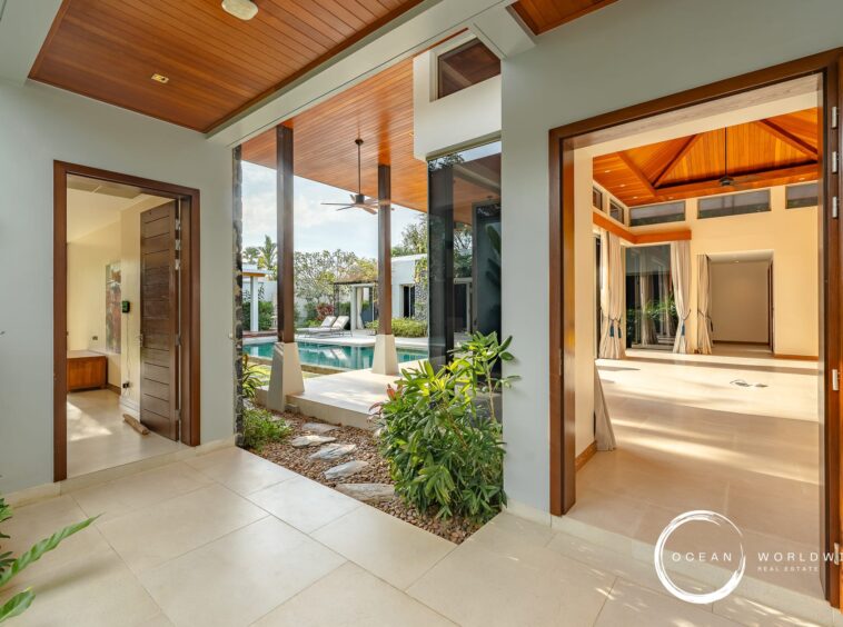 Open doorway to a sunny villa courtyard with a pool, wooden ceiling, and lounge chairs visible outside.