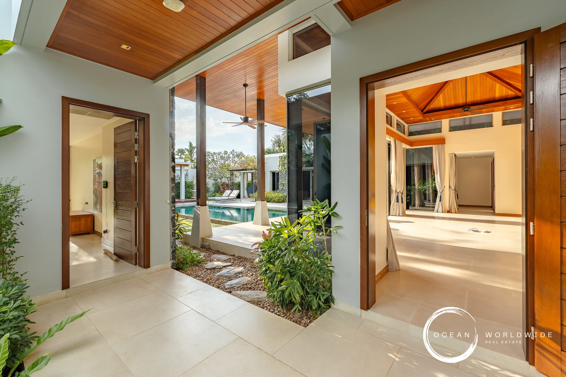 Open doorway to a sunny villa courtyard with a pool, wooden ceiling, and lounge chairs visible outside.