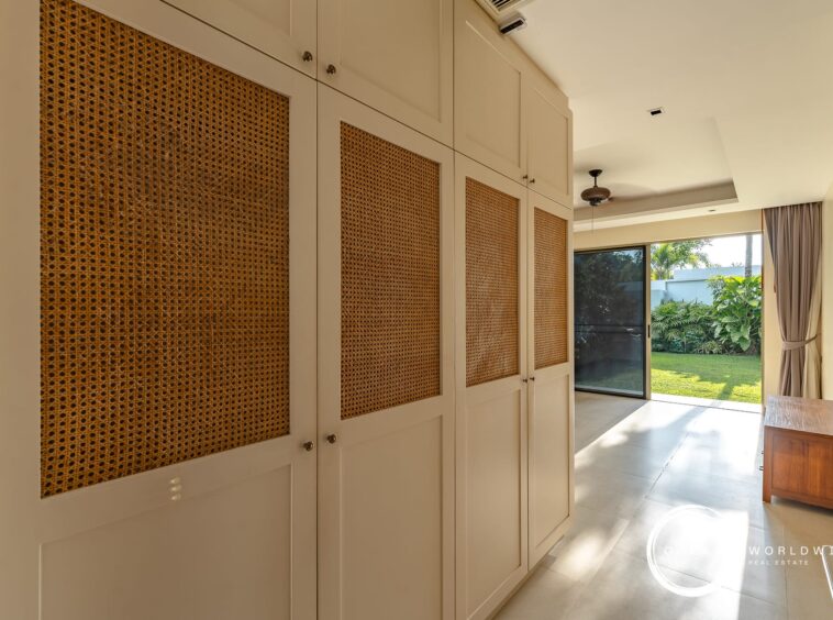 Built-in white cabinets with woven rattan panels line a sunlit hallway leading to a backyard garden window/door.