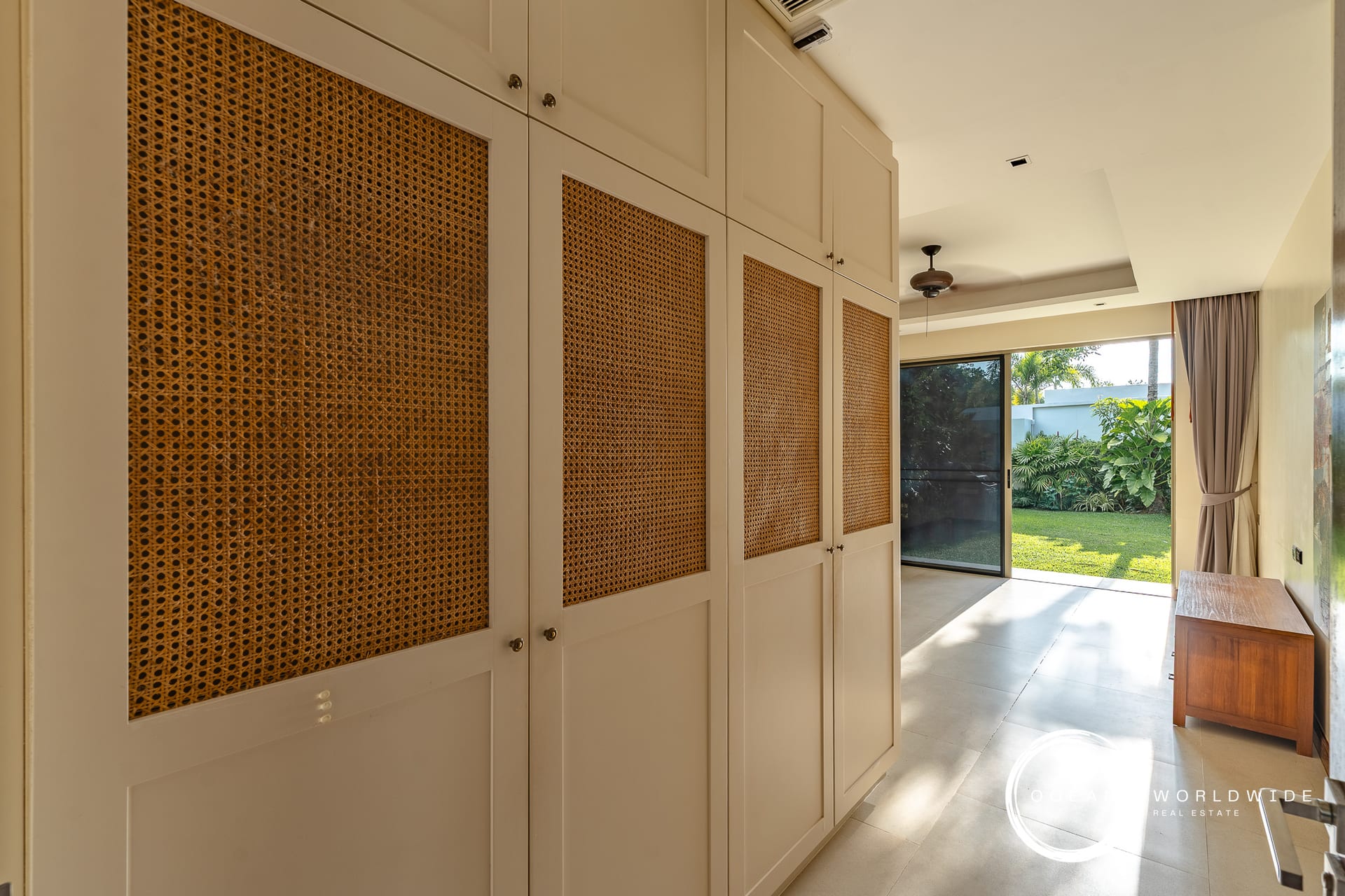 Built-in white cabinets with woven rattan panels line a sunlit hallway leading to a backyard garden window/door.