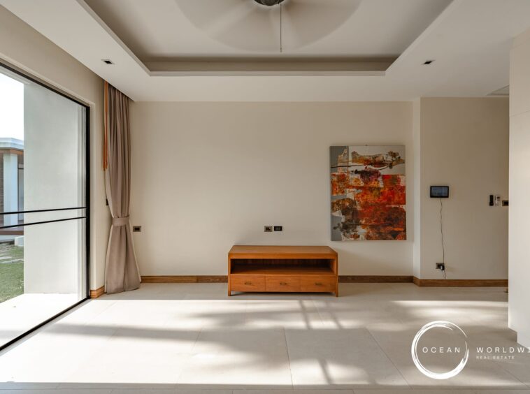 Bright, minimalist living room with a large glass sliding door, beige walls, and a wooden media console beneath an abstract painting.