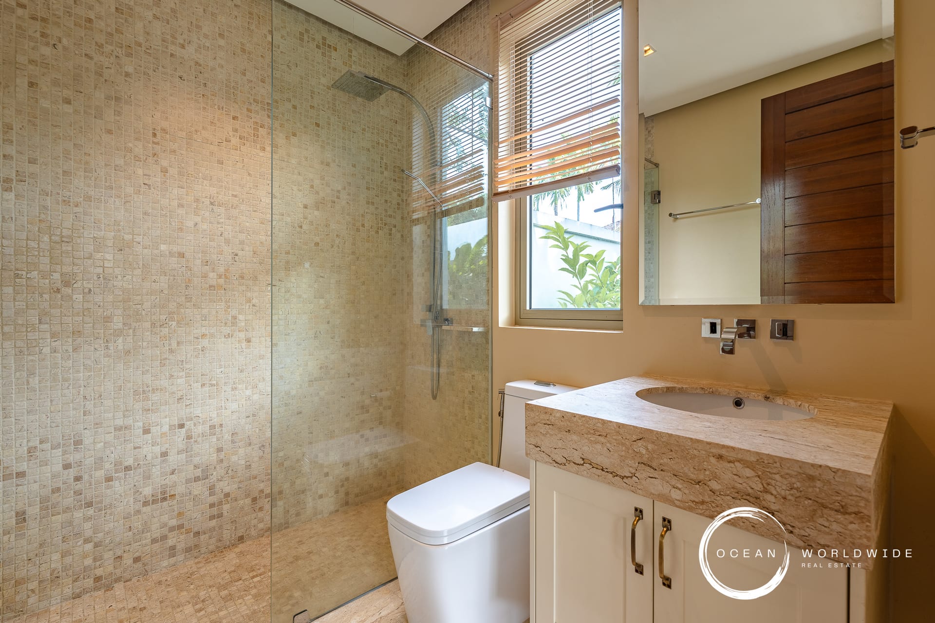 Modern bathroom with a glass-enclosed shower, beige mosaic tiles, and a white vanity.