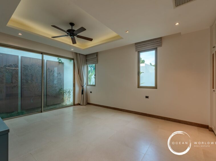 Modern minimalist living room with a ceiling fan, recessed lighting, and large sliding glass doors to an outdoor area. The room is unfurnished with light tile flooring and built-in white cabinets along one wall.