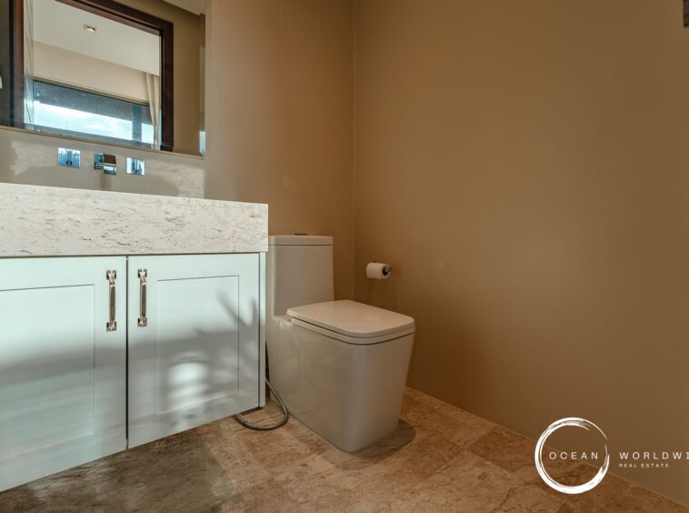 Modern bathroom with a light blue vanity, marble countertop, and a white toilet, glossy chrome fixtures, and a beige wall. Ocean Worldwide logo in corner.