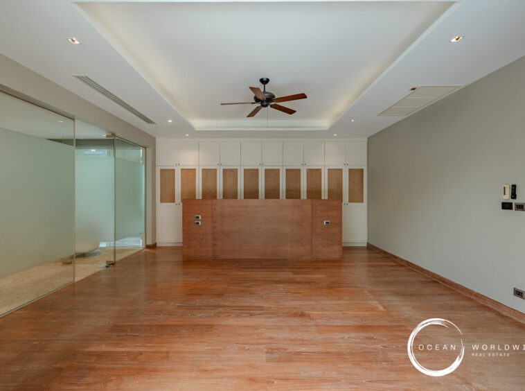 Modern office reception area with white built-in cabinets and a wooden counter, glass partition on the left, and a ceiling fan above.