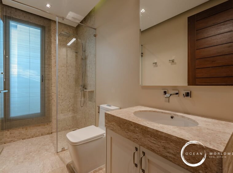 Modern bathroom with a glass-enclosed walk-in shower, beige tiled walls, and a marble countertop vanity.