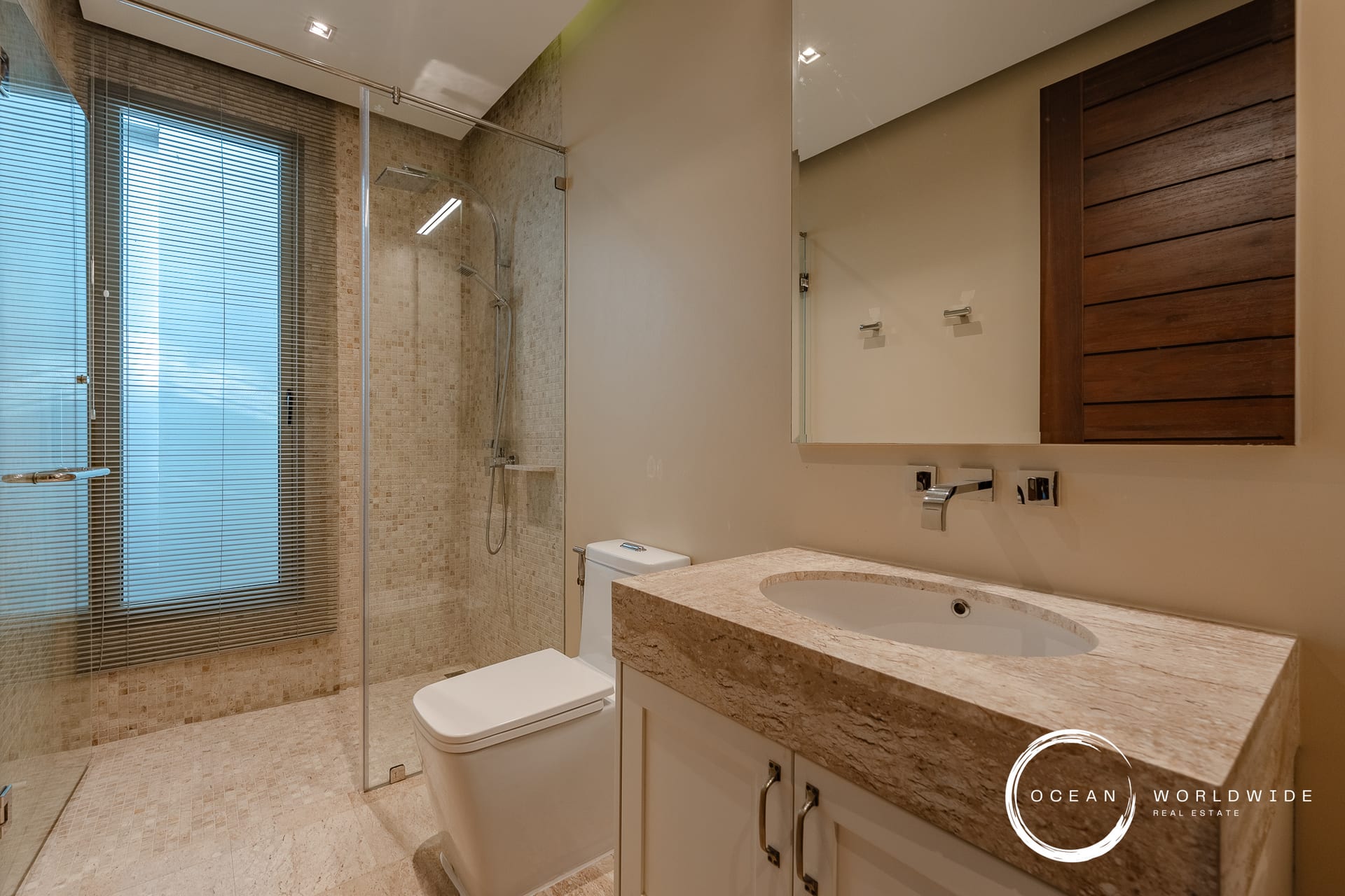Modern bathroom with a glass-enclosed walk-in shower, beige tiled walls, and a marble countertop vanity.