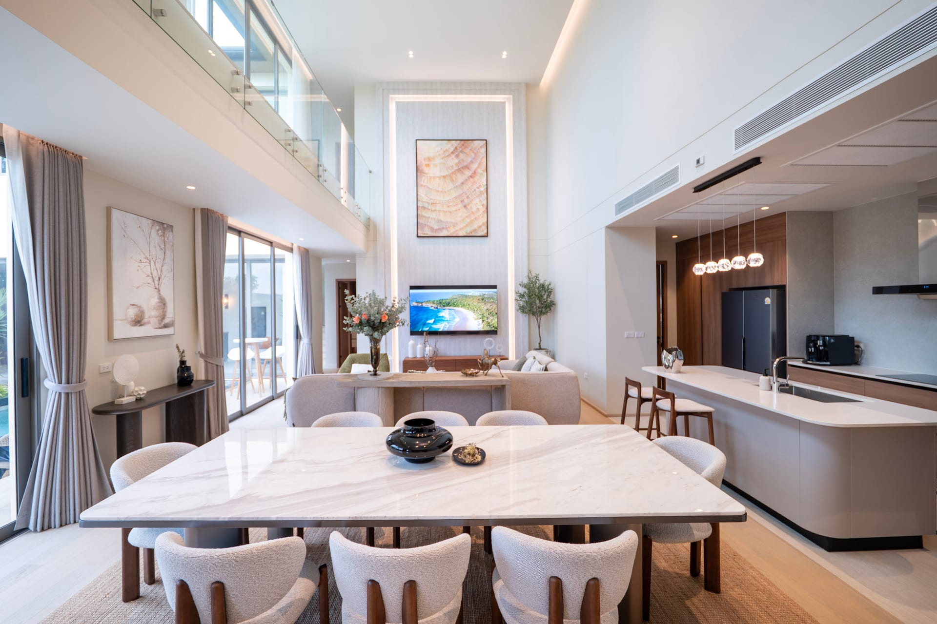 Open-plan living and dining area with a marble-topped table, beige chairs, and a kitchen island in a bright, modern home.