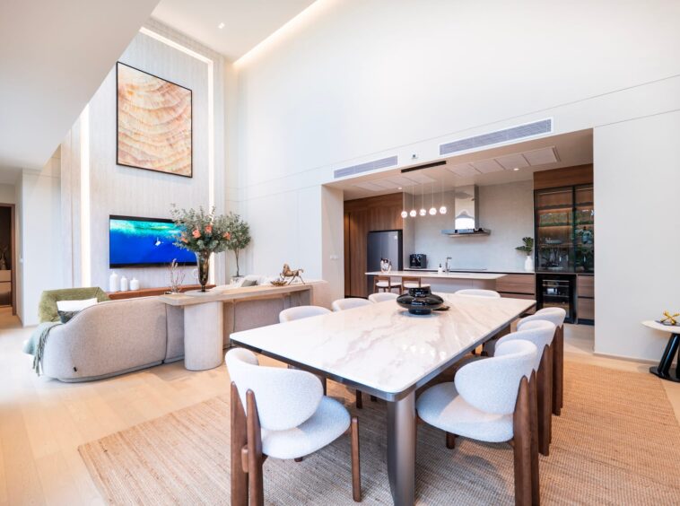 Open-concept living area with a marble dining table, beige chairs, and a modern kitchen in the background.