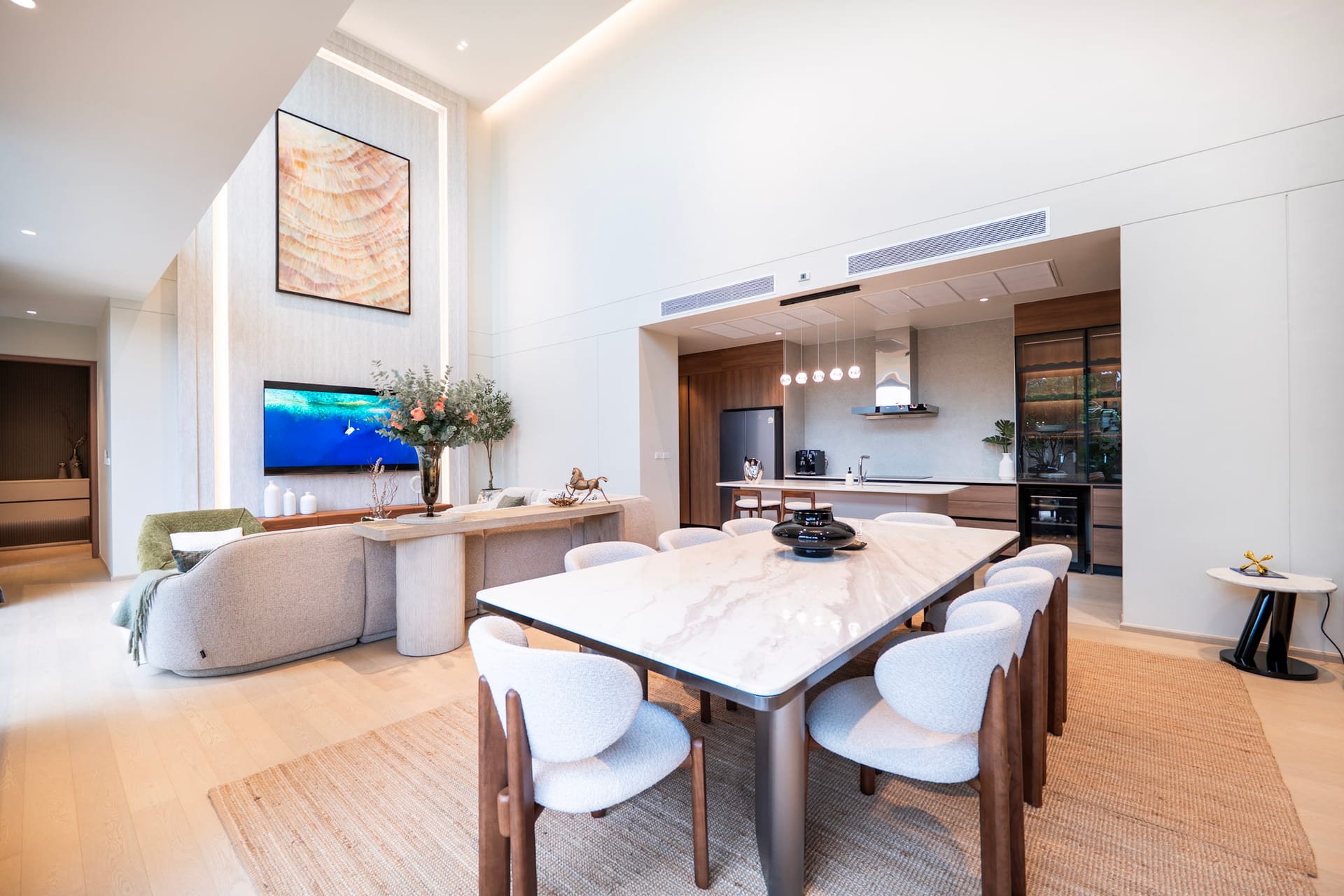 Open-concept living area with a marble dining table, beige chairs, and a modern kitchen in the background.