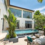 Modern two-story home courtyard with large glass doors, pool, and tropical plants under a blue sky