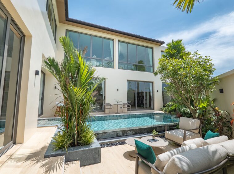 Modern two-story home courtyard with large glass doors, pool, and tropical plants under a blue sky