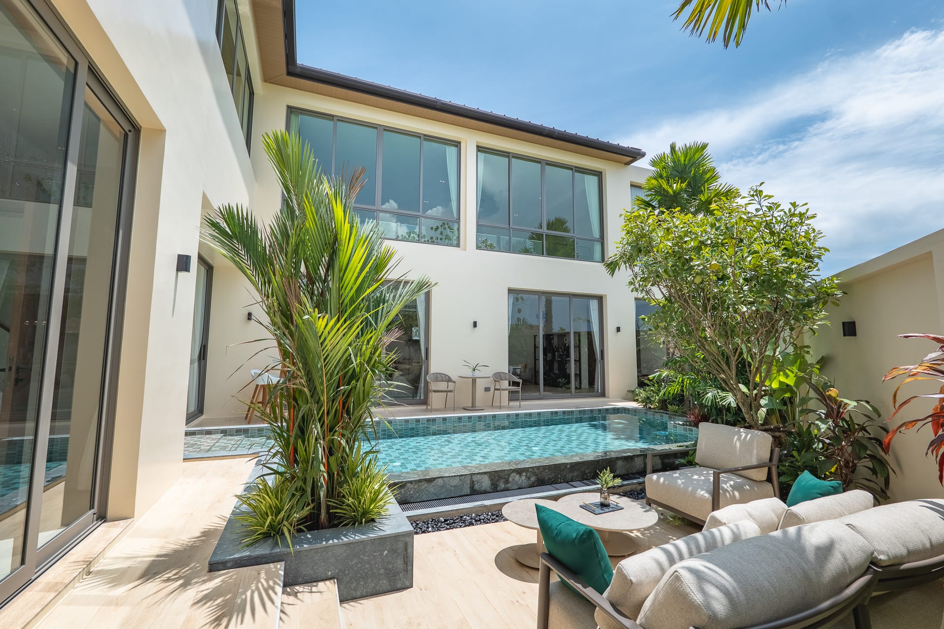 Modern two-story home courtyard with large glass doors, pool, and tropical plants under a blue sky