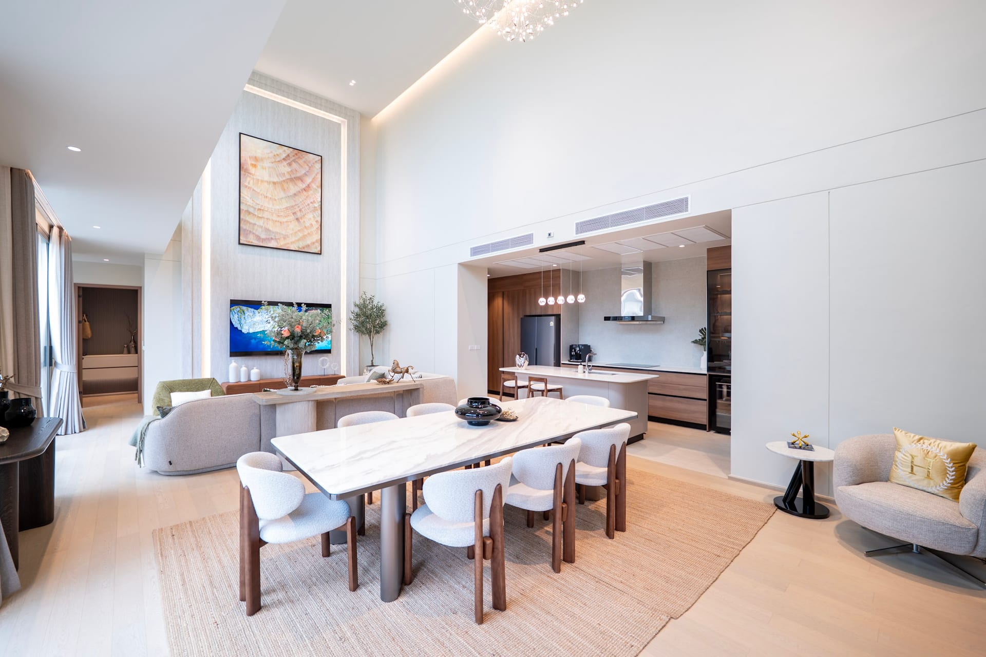Bright open-plan living, dining, and kitchen area with marble dining tables, light wood floors, and soft beige seating.