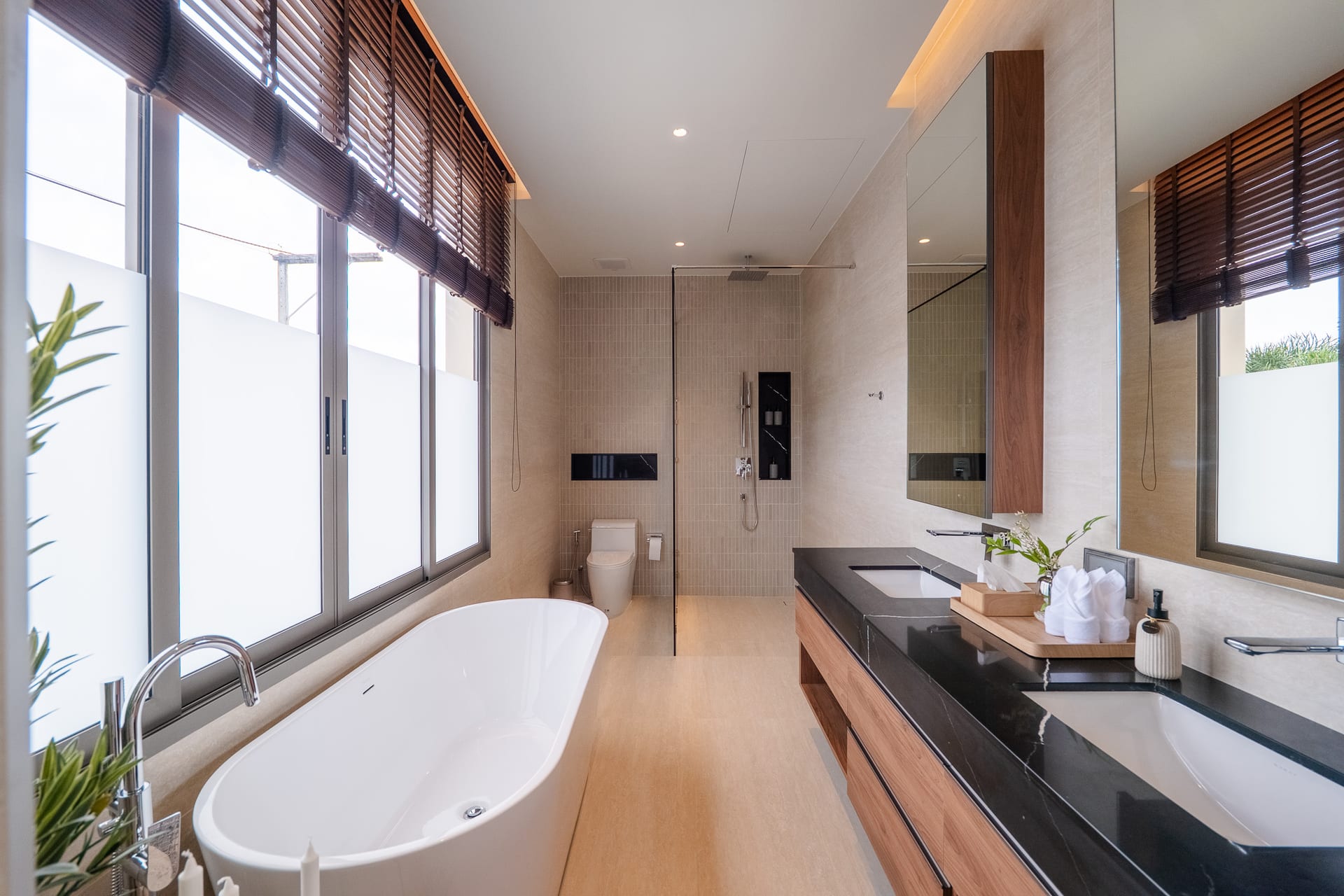 Bright contemporary bathroom with a freestanding white tub by large frosted windows, a glass-enclosed shower, and a long black marble vanity top with wood drawers.