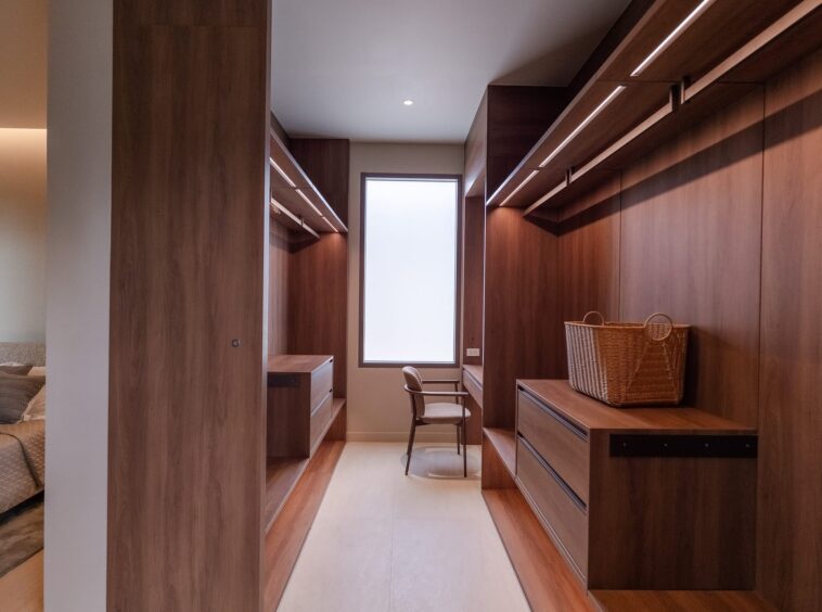 Wood-paneled walk-in closet with built-in storage on both sides, a central window, and a wicker basket on a dresser/console.