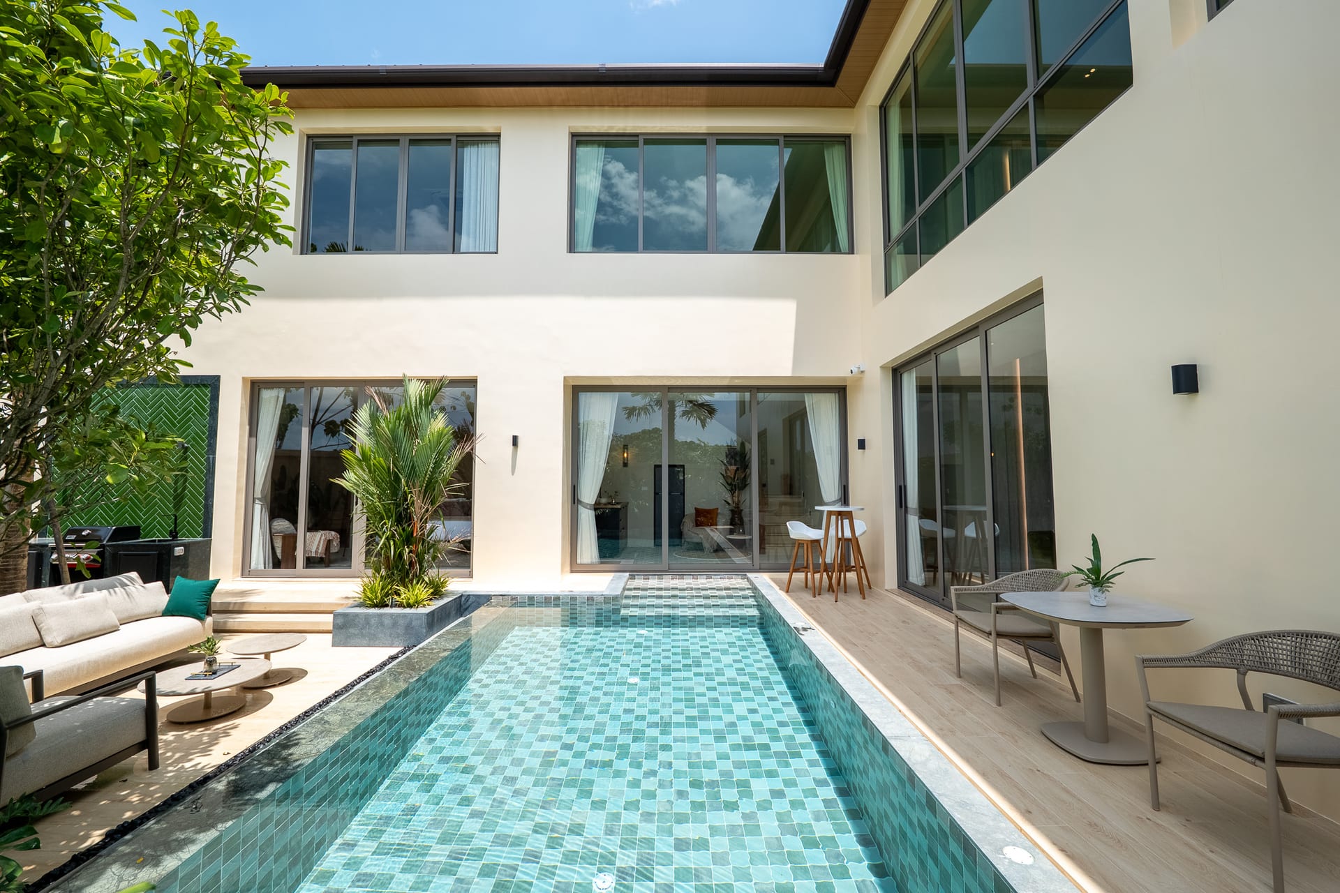 Contemporary two-story house with large glass doors, a turquoise tiled pool, and outdoor seating on a wooden deck.
