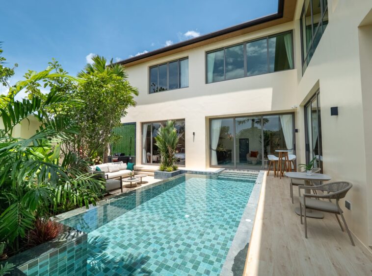 Modern villa courtyard with a turquoise tiled rectangular pool, lush tropical plants, and glass doors.