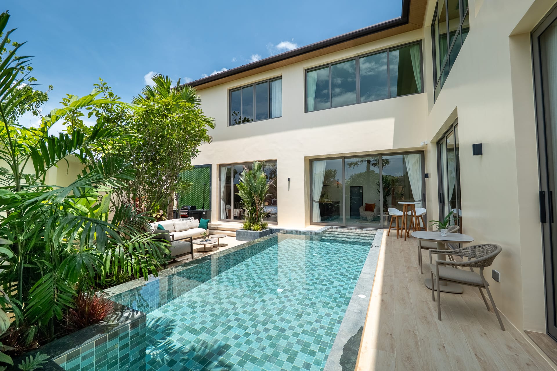 Modern villa courtyard with a turquoise tiled rectangular pool, lush tropical plants, and glass doors.