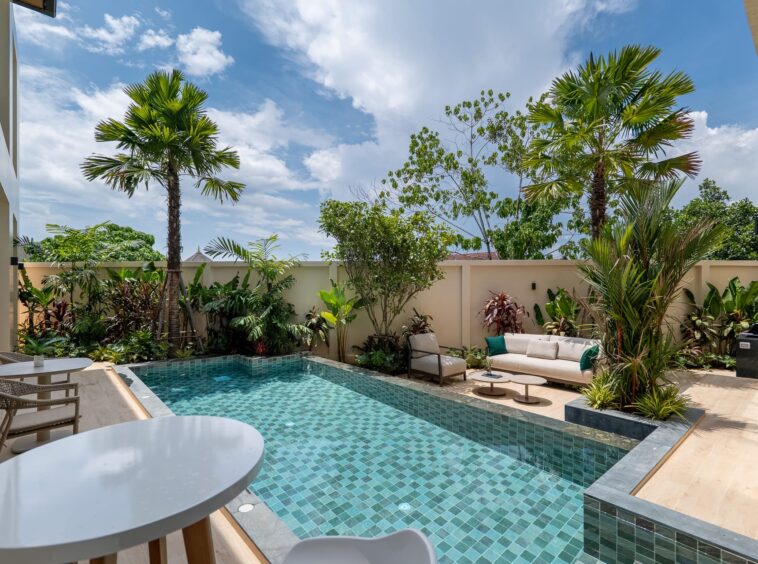 Modern backyard with a rectangular turquoise-tiled pool, cream seating, and tropical plants.
