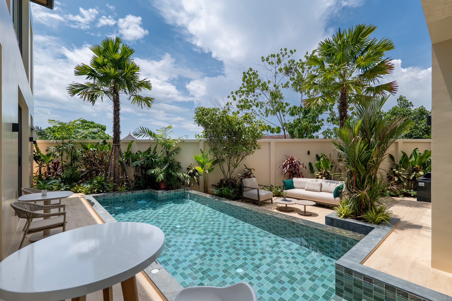Modern backyard with a rectangular turquoise-tiled pool, cream seating, and tropical plants.