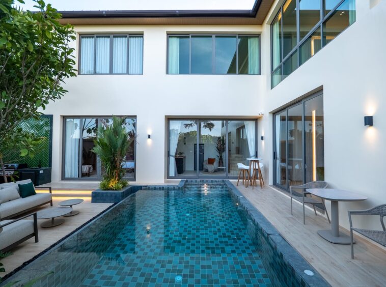 Modern courtyard pool with blue mosaic tiles, lounge seating, and glass doors opening to indoors