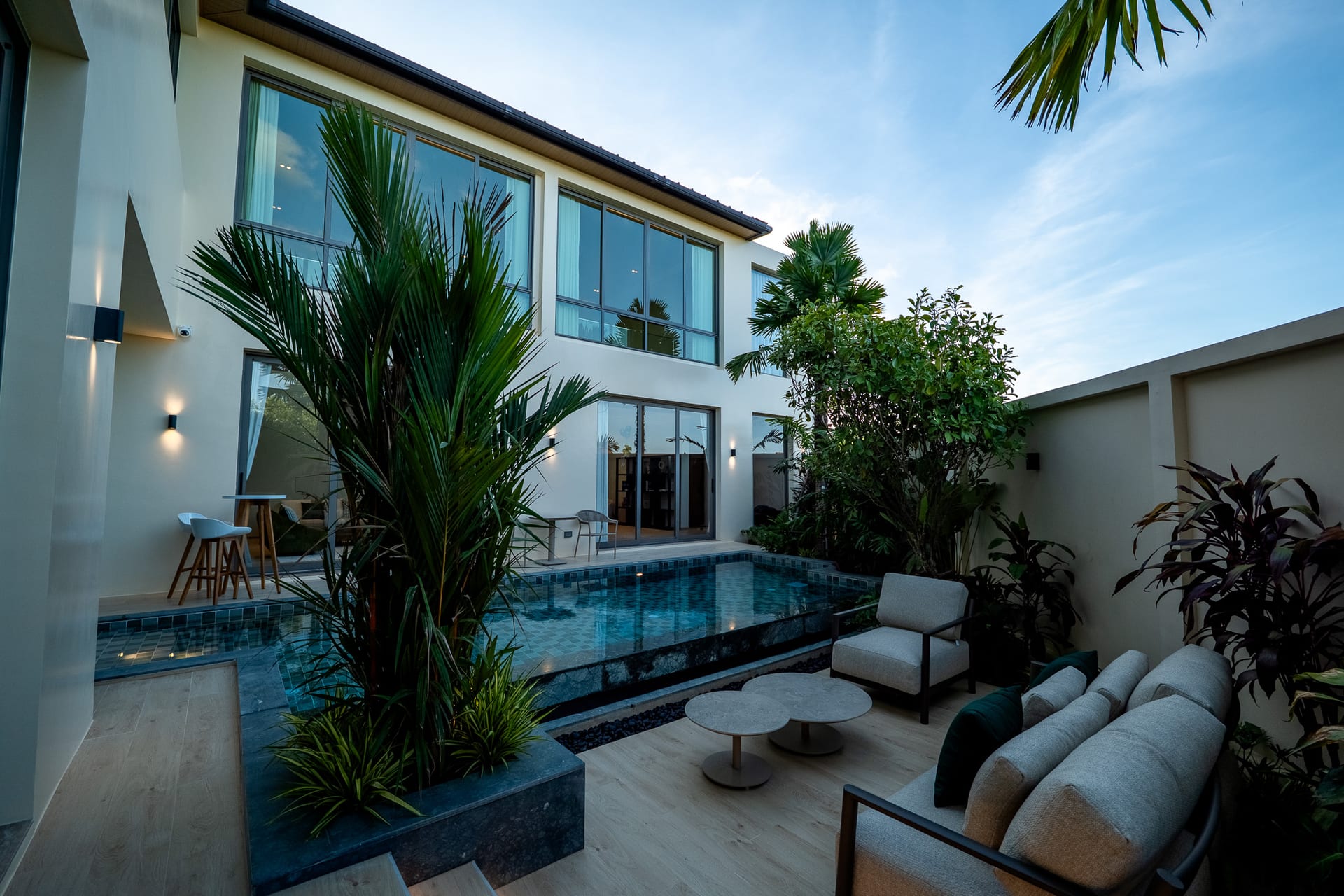 Modern two-story house with glass doors, pool, and tropical plants in a courtyard