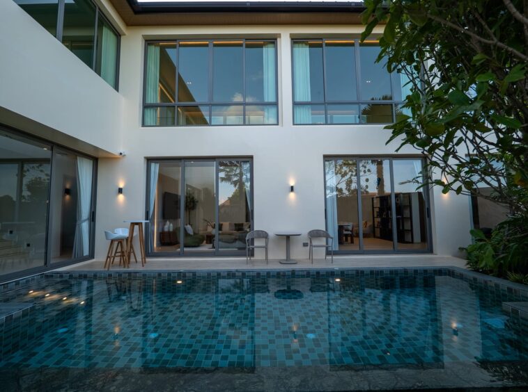 Modern backyard with a blue-tiled pool in front of a white contemporary house and glass sliding doors.