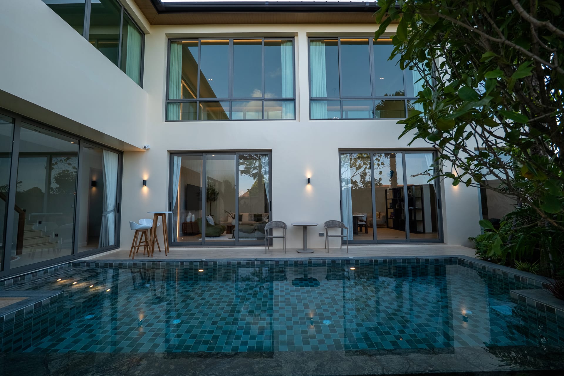 Modern backyard with a blue-tiled pool in front of a white contemporary house and glass sliding doors.
