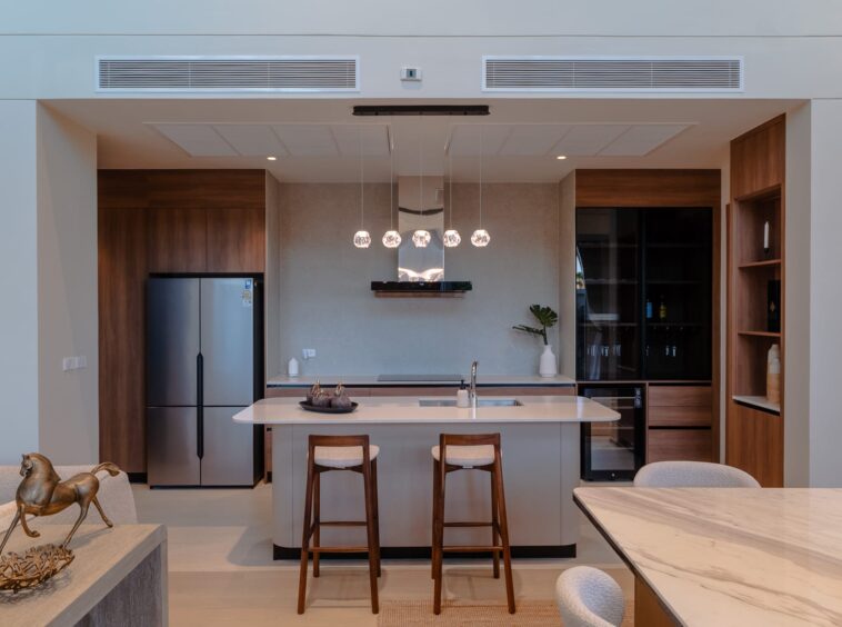 Open-concept kitchen with island, pendant lights, and wooden bar stools facing a marble countertop.