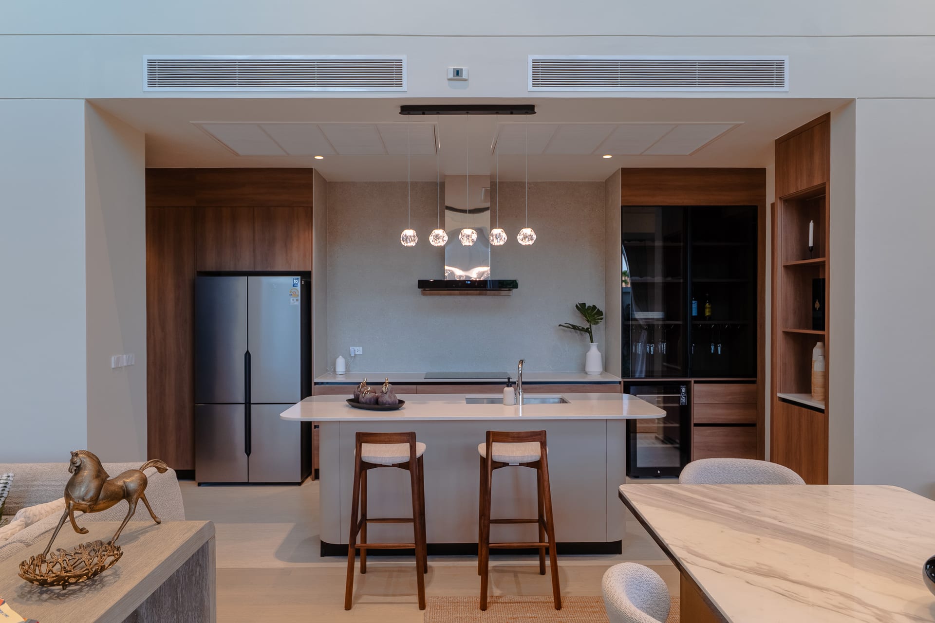 Open-concept kitchen with island, pendant lights, and wooden bar stools facing a marble countertop.