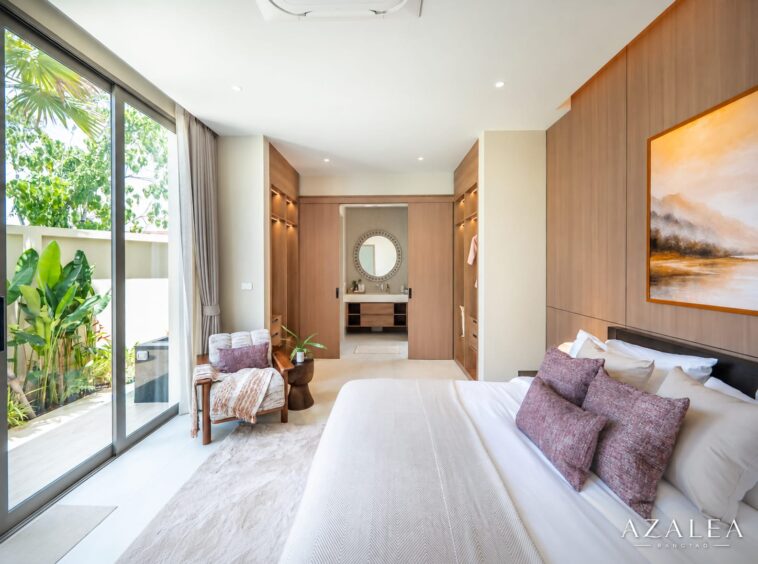 Luxurious hotel bedroom with a king bed, white linens, purple pillows, wood-paneled walls, and large glass doors to greenery outside.