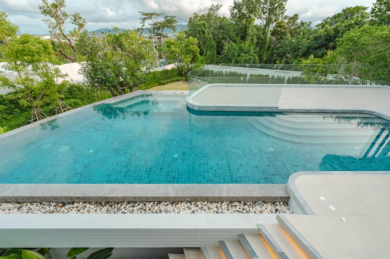 Modern outdoor infinity pool with turquoise water, glass railing, and lush trees in the background