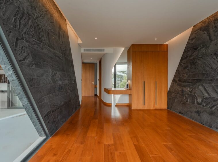 Modern hallway with dark stone walls, warm wood floor, and a tall wooden wardrobe with long metal handles.