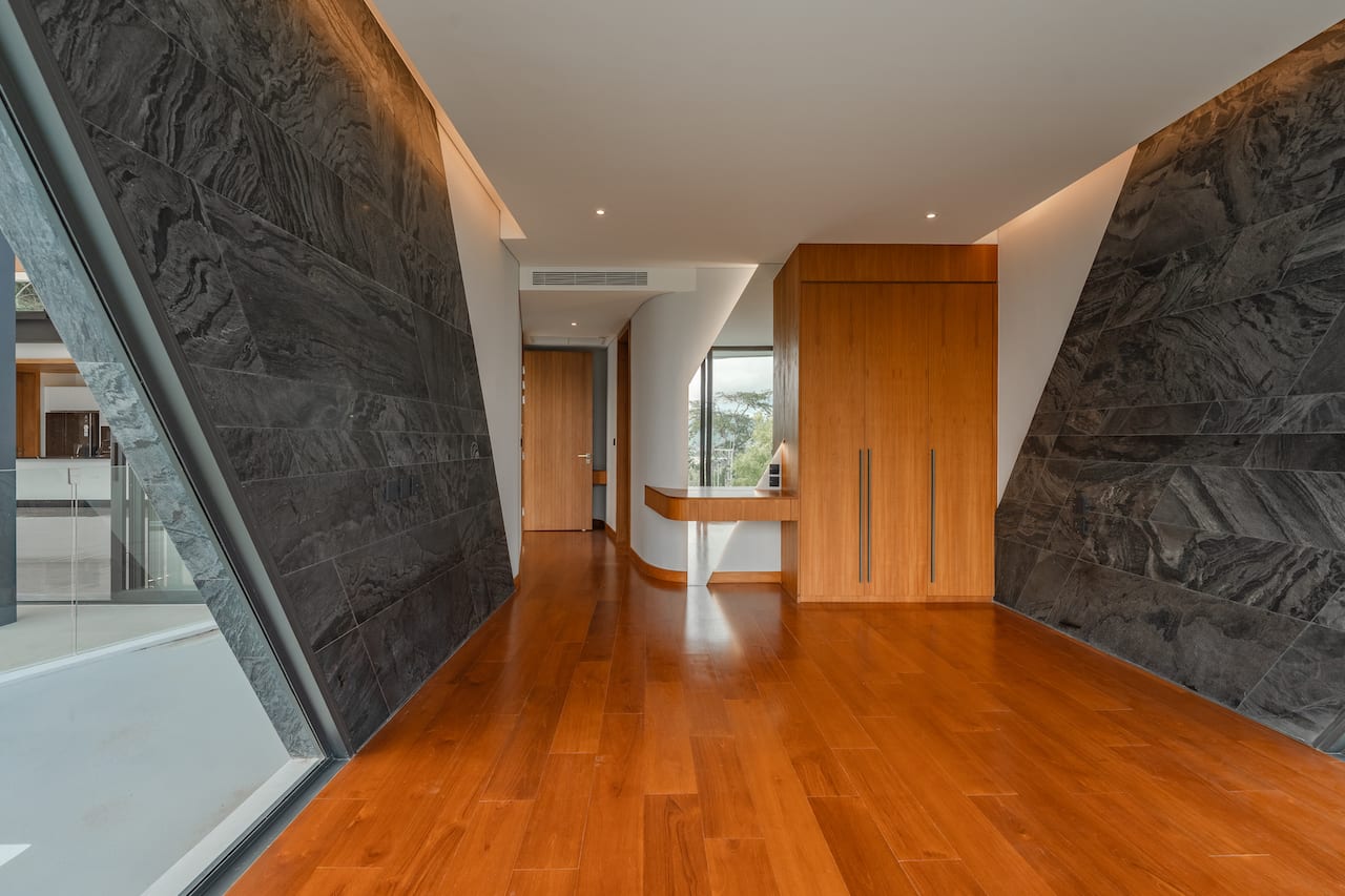 Modern hallway with dark stone walls, warm wood floor, and a tall wooden wardrobe with long metal handles.