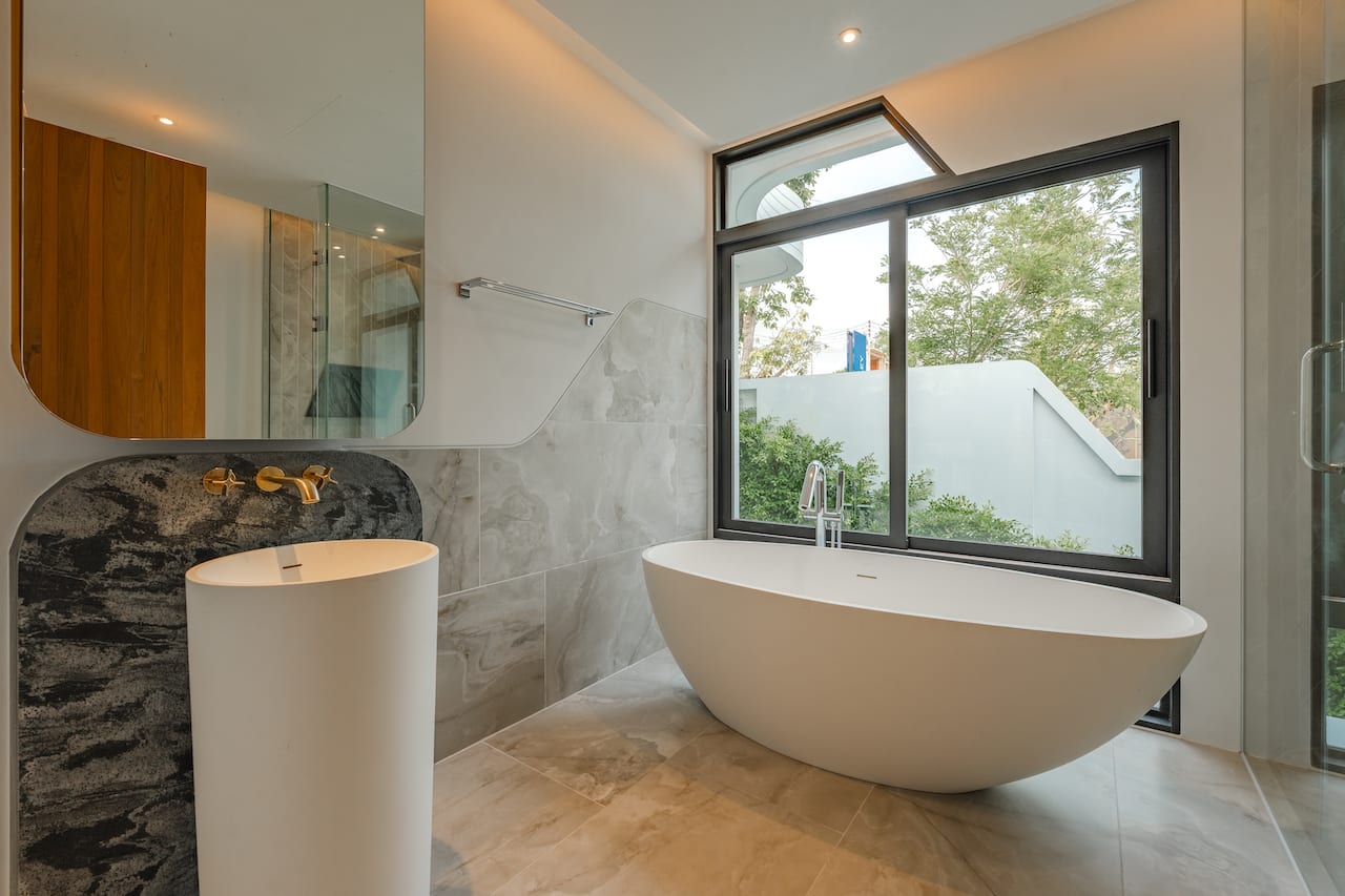 Modern bathroom with a freestanding oval tub by a large window and marble-tiled walls and floor