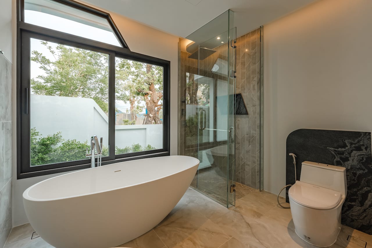 Modern bathroom with a freestanding oval tub by a large window, a glass shower enclosure, and a toilet in a bright, contemporary space.