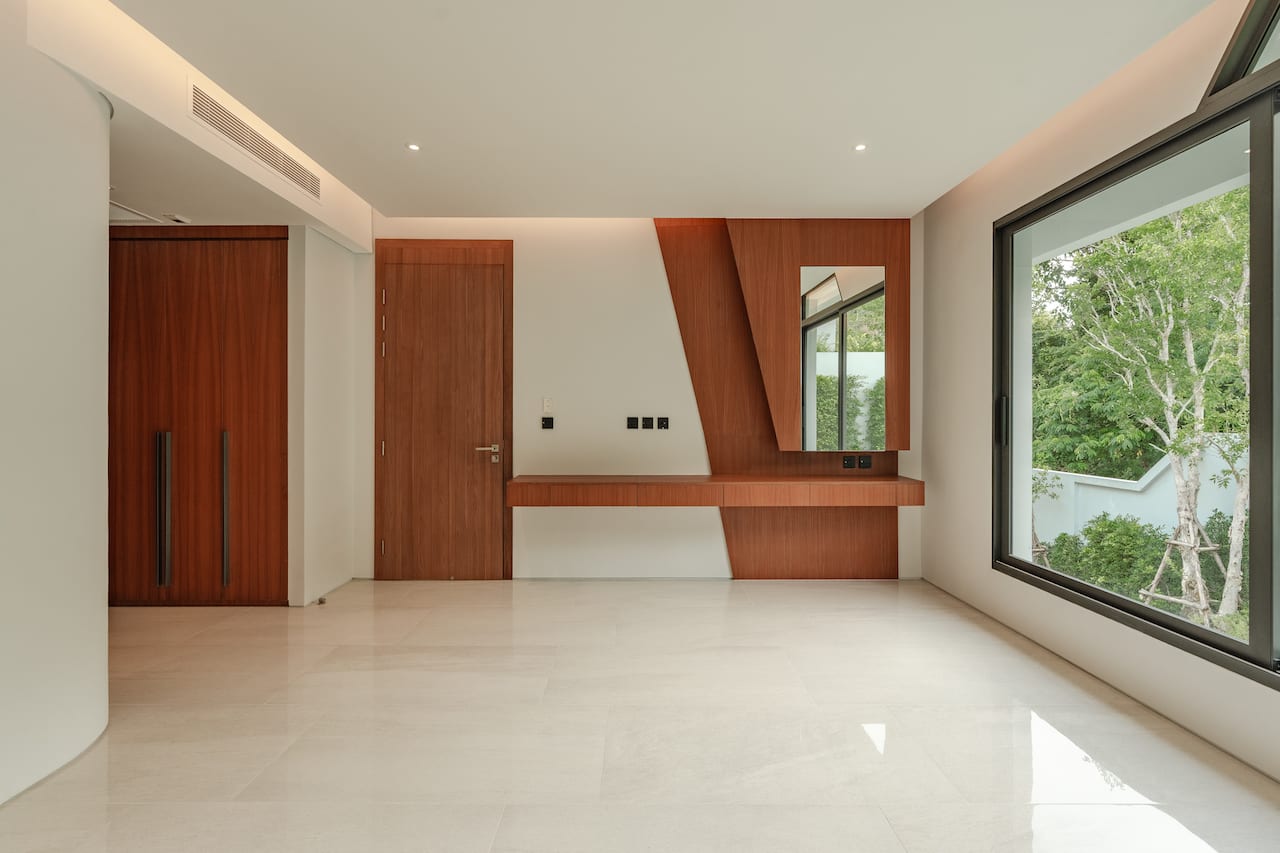 Modern living space with a wooden built-in desk, mirror and large window overlooking greenery outside.