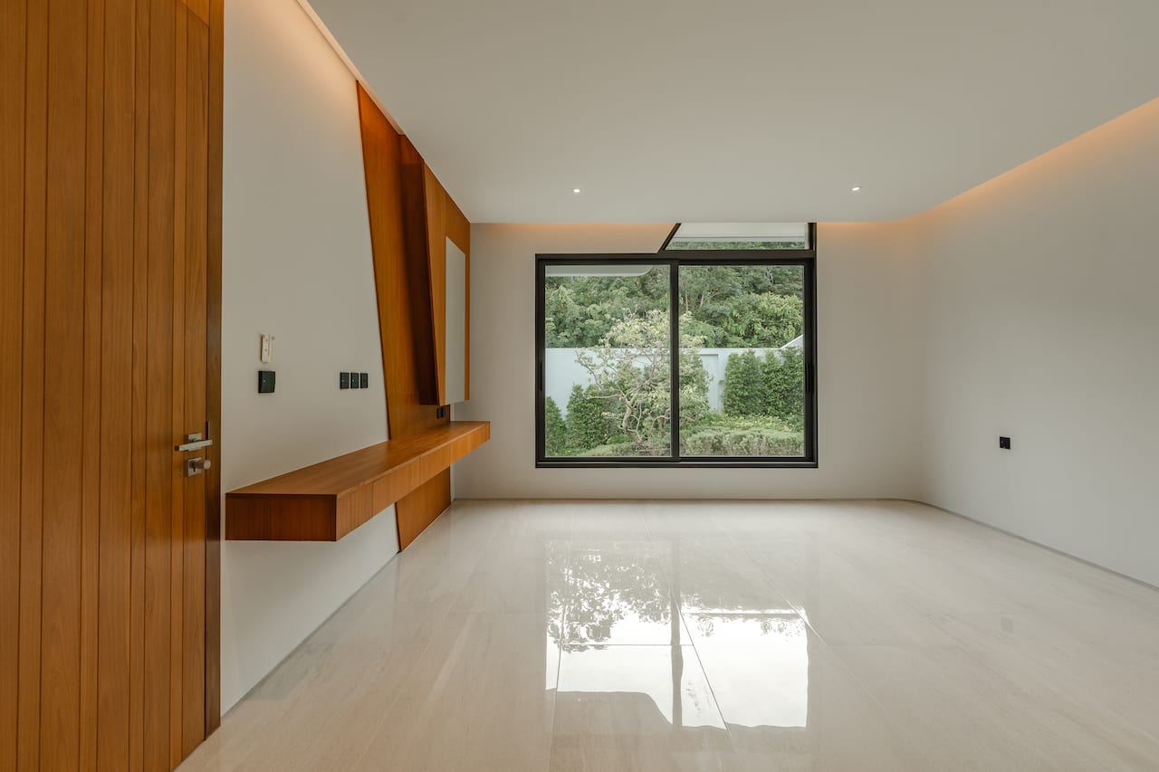 Modern empty room with white glossy floor, wood-paneled wall and floating desk, large window overlooking greenery.