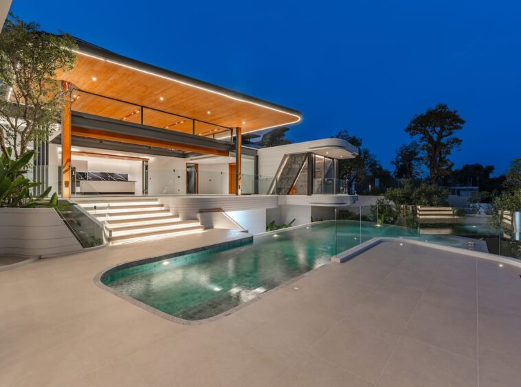 Modern luxury home with illuminated outdoor pool area at dusk and a glass railing patio.”,