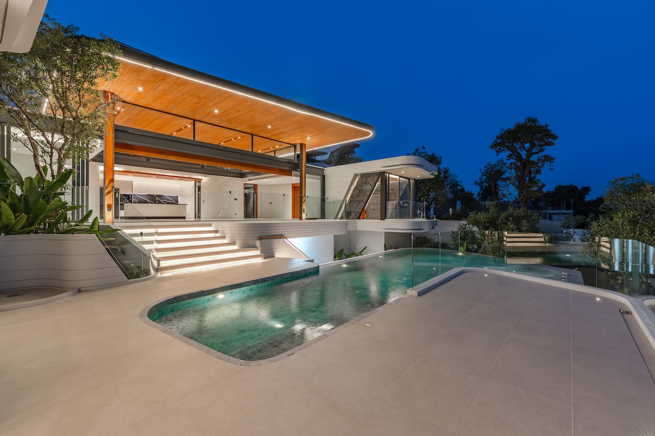 Modern luxury home with illuminated outdoor pool area at dusk and a glass railing patio.”,