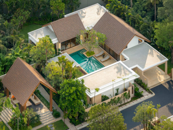 Aerial view of a modern villa with brown-tiled roofs, a rectangular pool, and tropical landscaping surrounding it.