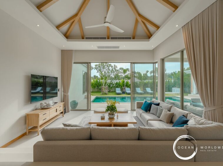 Bright living room with beige sectional facing sliding glass doors to a pool yard, vaulted ceiling with wooden beams and a white ceiling fan.
