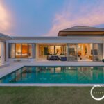 Modern luxury villa with a rectangular turquoise pool, glass walls, and open living spaces at sunset. Ocean Worldwide branding visible.